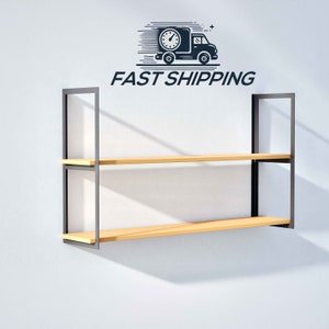 May include: A black metal shelf unit with two wooden shelves. The shelf unit is mounted on a white wall. The text "FAST SHIPPING" is printed above the shelf unit.