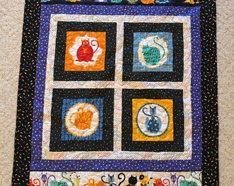 May include: A black and white quilt with a colorful cat design. The quilt features four squares with different colored cats in the center of each square. The quilt is surrounded by a black border with a row of colorful cats along the top and bottom.