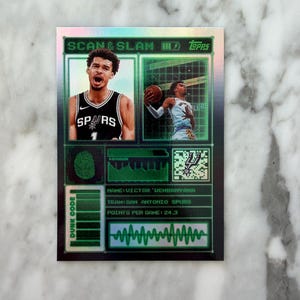 May include: A holographic basketball card with the text "SCAN & SLAM" and "TOPPS". The card features two images of basketball players, the Spurs logo, and the text "DUNK CODE". The card also includes the name "VICTOR 'WEMBANYAMA" and "POINTS PER GAME: 24,3".