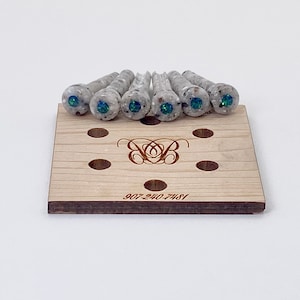 May include: Set of eight white guitar tuning pegs with iridescent green and blue accents. The pegs are displayed on a wooden stand with a logo and phone number.