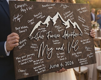 May include: A wooden wedding sign with the words "Our Forever Adventure" and the names "Meg and Val" in elegant script. The sign features a mountain range design and is signed by guests. The date "June 6, 2026" is also displayed.