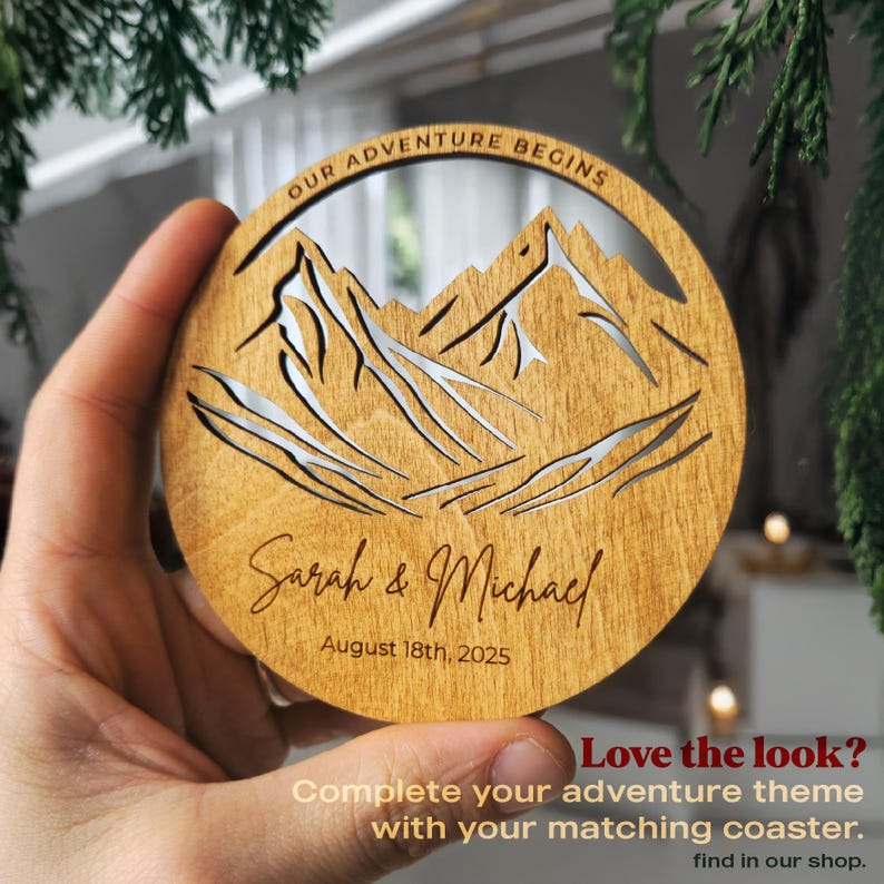 Personalized wooden wedding coaster with mountain design and “Our Adventure Begins” engraving, custom names and date, rustic wood wedding favor matching adventure theme guest book.