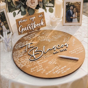 Rustic wooden wedding guestbook sign on table with please sign our guestbook sign, personalized round wood guest book alternative with engraved names and guest messages.