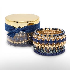 May include: A set of stacked bracelets in a clear jar with a gold lid and a navy blue bow. The bracelets are a mix of gold, navy blue, and crystal beads. The bracelets are also stacked next to the jar.