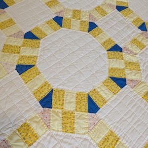 May include: Close-up of a handmade quilt with a repeating pattern of interlocking rings. The quilt features a white background with yellow floral print and blue accents. The quilt is quilted with a diamond pattern.