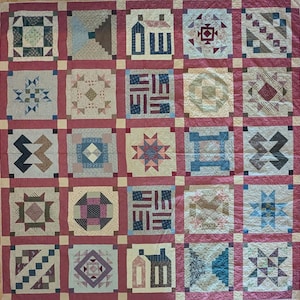 May include: A handmade quilt featuring a patchwork design with various geometric patterns. The quilt showcases squares in shades of blue, green, pink, and beige, framed by a red border. The quilt is a traditional craft item.