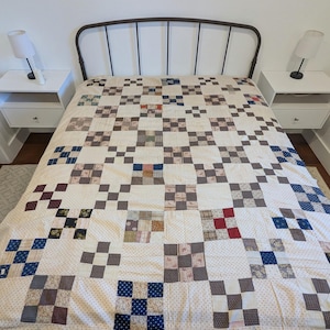 May include: A patchwork quilt featuring a repeating nine-patch block pattern. The quilt is constructed from various fabric squares in shades of blue, red, brown, and cream, interspersed with cream-colored fabric squares featuring a small red dot pattern.