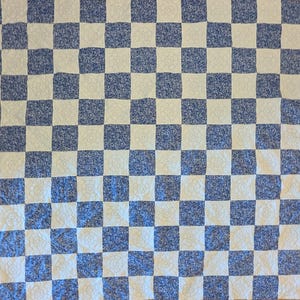 May include: A blue and white checkered quilt. The squares alternate between a solid blue pattern and a white floral design. The quilt is made of a soft, textured fabric.