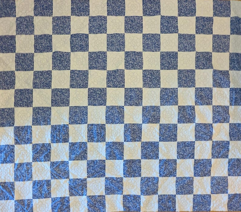 May include: A blue and white checkered quilt. The squares alternate between a solid blue pattern and a white floral design. The quilt is made of a soft, textured fabric.