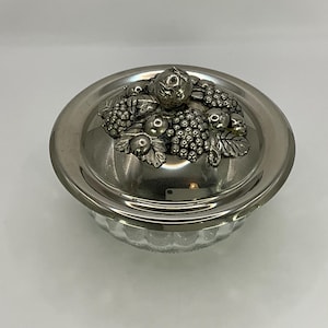 Könnte beinhalten: Eine versilberte Glasschüssel mit einem Deckel, der mit einem detaillierten Fruchtmuster verziert ist. Der Deckel ist mit Trauben, Beeren und Blättern verziert und bildet ein dekoratives und elegantes Mittelstück.