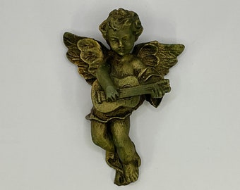 May include: A green cherub figurine playing a guitar. The figurine is made of a smooth, textured material and has a detailed design.
