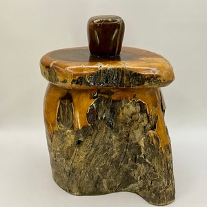 May include: A wooden box with a natural wood finish and a unique, irregular shape. The lid is made of a smooth, dark wood and has a rounded top. The box is perfect for storing small items or trinkets.