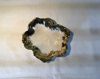Puede incluir: Un plato de cerámica blanca con un borde dorado y un diseño en forma de flor. El plato está sobre un fondo blanco.
