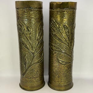 May include: A pair of brass vases with a floral design. The vases are made from repurposed artillery shells.