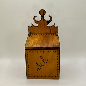 May include: A wooden salt box with a decorative top and a black painted inscription that reads "salt".