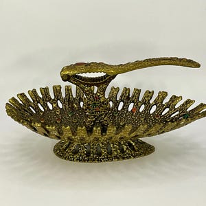 Peut inclure: Un casse-noisette en métal doré avec un design décoratif et orné. Le casse-noisette a un petit bol pour contenir les noix et un levier pour les casser. Le bol et le levier sont décorés de pierres précieuses colorées.