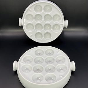 Op de afbeelding: Twee witte keramische schalen met 12 afzonderlijke ronde verdiepingen voor het serveren van escargots of andere kleine gerechten. De schalen hebben handvatten aan de zijkanten.