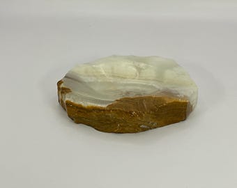 Puede incluir: Un plato de piedra natural blanco y marrón de forma irregular. El plato está hecho de ónix y tiene una superficie lisa y pulida.