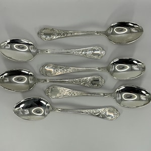 Puede incluir: Seis cucharaditas de plata con mangos adornados y un acabado pulido. Las cucharaditas están dispuestas en fila, con los mangos apuntando hacia la derecha.