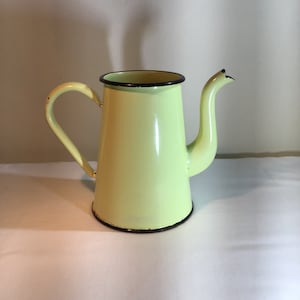 Può includere: Una teiera di smalto giallo pallido con un bordo nero e un beccuccio. La teiera ha un manico sul lato.