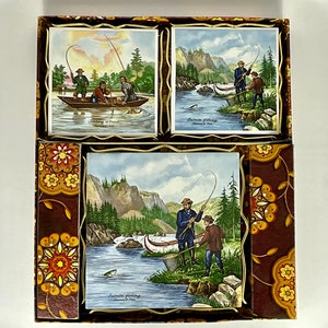 May include: A set of three vintage ceramic tiles depicting scenes of salmon fishing in a river. The tiles are framed in gold and have a brown background with floral patterns. The tiles feature illustrations of people fishing in a river with mountains and trees in the background. The text on the tiles reads "Salmon Fishing, Canadian Rockies".