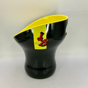 Puede incluir: Hielera negra y amarilla con un diseño curvo. El interior es de color amarillo brillante, contrastando con el exterior negro. Una etiqueta amarilla con texto rojo y negro está adherida al frente. La hielera tiene una abertura ancha y una base redondeada.