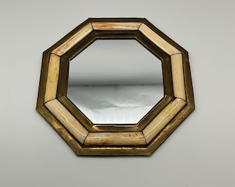 May include: Octagonal mirror with a brass frame and cream-colored accents. The mirror's shape is geometric, with a reflective surface. The frame has a vintage or antique appearance, adding a touch of elegance to the design.