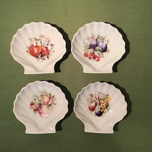 May include: Set of four white ceramic shell-shaped dishes with painted fruit designs. Each dish features a different fruit combination, including apples, plums, cherries, peaches, and grapes.
