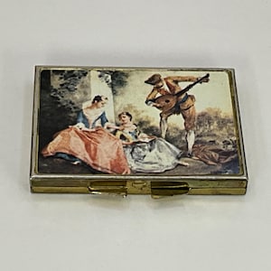 Vintage metal pocket pill box / trinket box with an old picture of a painting on the front.