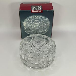 May include: A clear glass trinket box with a starburst pattern. The box is closed and sitting on a white surface. The box is in its original packaging, which is red and blue and says "Fine Italian Style" and "Coveltro Fine Italian Glassware".
