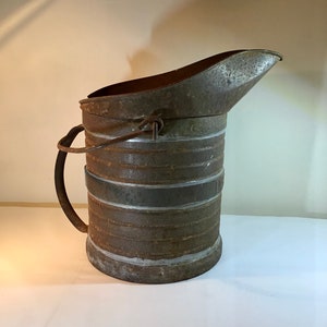 Może przedstawiać: Wodoodporna konewka z metalu w stylu vintage z wylewką i uchwytem. Konewka jest zardzewiała i ma etykietę z napisem "12 Gal."