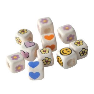 May include: A collection of white, square beads with various colorful designs. The beads feature images of flowers, hearts, and smiley faces. The designs are in yellow, orange, pink, blue, and purple.