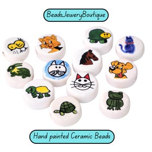 May include: Hand-painted ceramic beads with various animal designs, including a cat, dog, turtle, and frog. The beads are white with colorful illustrations and the text "BeadsJeweryBoutique" and "Hand painted Ceramic Beads".