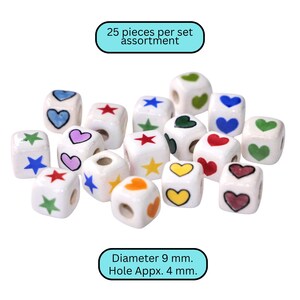 May include: A collection of 25 white ceramic cube beads, each adorned with colorful heart, star, and other geometric designs. The beads have a diameter of 9 mm and a hole of approximately 4 mm.