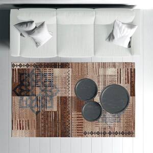 Può includere: Vista dall'alto di un salotto con un divano bianco con cuscini, un tappeto fantasia e tre tavolini rotondi grigio scuro. Il tappeto presenta un design geometrico nei toni del marrone, beige e blu.