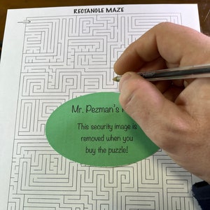 May include: A black and white rectangle maze puzzle with the text "RECTANGLE MAZE" at the top. A green oval sticker with the text "Mr. Pezman's" and "This security image is removed when you buy the puzzle!" is partially covering the maze.