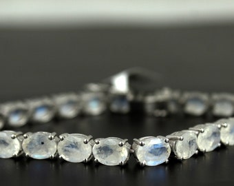 Puede incluir: Un brazalete de plata con gemas de piedra lunar de forma ovalada. El brazalete está hecho de plata de ley y tiene un acabado pulido.