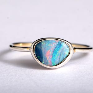 Puede incluir: Un anillo de plata con una piedra de ópalo. El ópalo muestra colores azules, verdes y rojos, engastado en un bisel. La banda es de plata pulida. Una joya que muestra los colores y el diseño del ópalo.