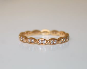 May include: A gold band ring with a row of small, clear diamonds set in a wavy pattern.