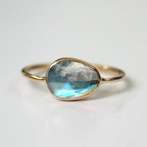 May include: A gold ring with a large, oval-shaped moonstone. The moonstone has a blue and iridescent sheen.