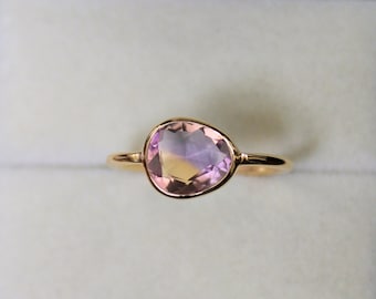 May include: A gold ring with a large, oval-shaped, light pink and purple gemstone.