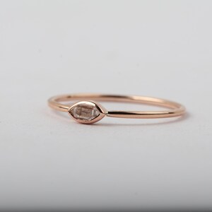 Puede incluir: Un delicado anillo de oro rosa con una pequeña piedra preciosa de forma marquesa transparente.