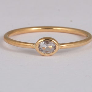 以下が含まれることがあります： ベゼルセットされた楕円形のダイヤモンドが特徴の繊細なゴールドリング。リングは細く磨かれたバンドとシンプルでエレガントなデザインです。ダイヤモンドの長さは約0.64cmです。