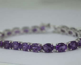 May include: A silver bracelet with a row of oval-shaped amethyst gemstones.