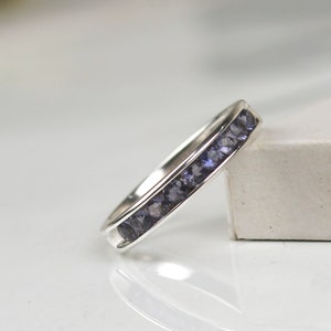 May include: A silver band ring with a row of small, dark purple gemstones.
