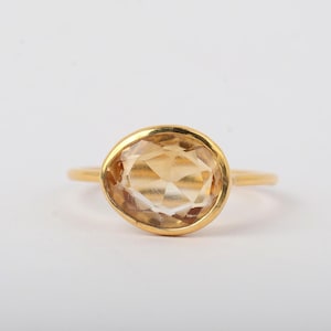 Peut inclure: Une bague en or avec une grande pierre précieuse jaune clair de forme ovale et à facettes, montée sur un anneau en or lisse et poli. La pierre présente une qualité transparente et claire avec de multiples facettes géométriques.