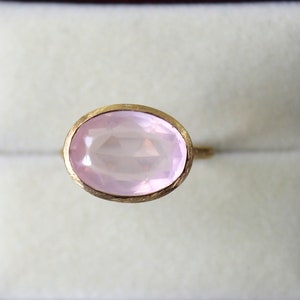 May include: A pink oval gemstone ring with a gold setting.