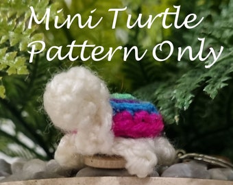 May include: A small crocheted turtle with a white shell and a colorful, striped, pink, blue, and green shell. The turtle is sitting on a wooden base and is surrounded by small rocks.