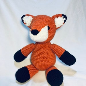 May include: A crocheted orange fox plush toy with black feet and white accents on the ears.