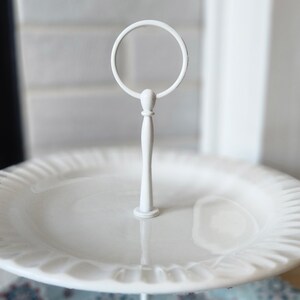 Peut inclure: Pr&eacute;sentoir &agrave; deux niveaux blanc avec une poign&eacute;e circulaire. Le pr&eacute;sentoir comprend une assiette en c&eacute;ramique blanche avec un bord festonn&eacute;. Le support central est une fine tige m&eacute;tallique blanche. Id&eacute;al pour pr&eacute;senter des desserts ou des amuse-gueules.
